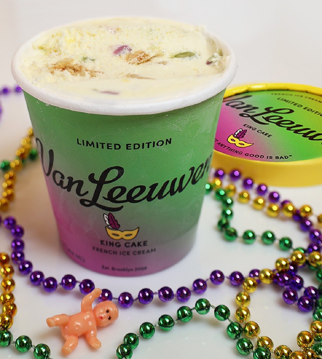 A pint of King Cake Ice Cream by Van Leeuwen surrounded by Mardi Gras beads and a king cake mini baby doll