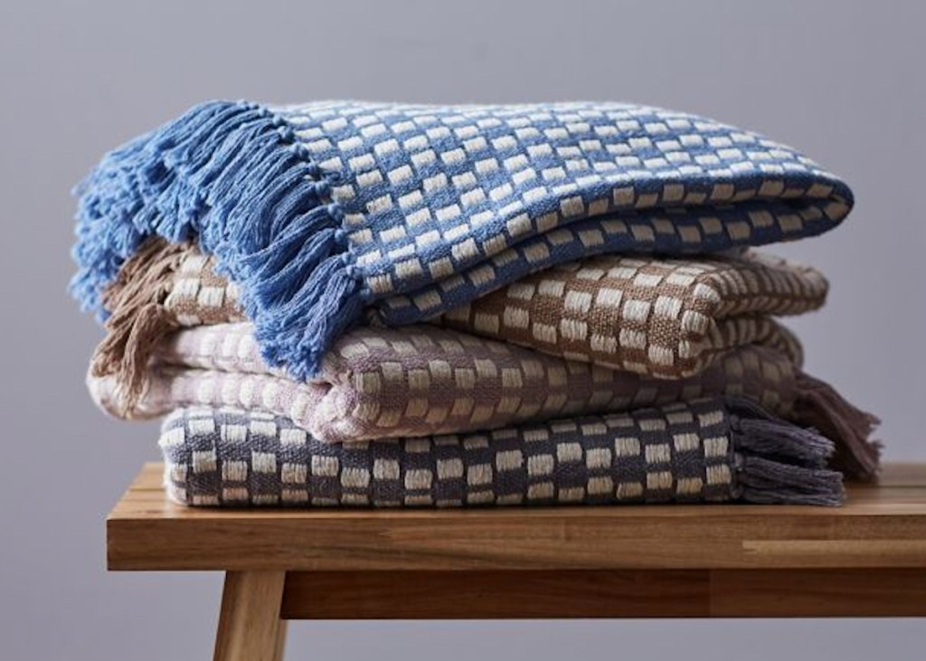 stack of knit blankets on wood bench