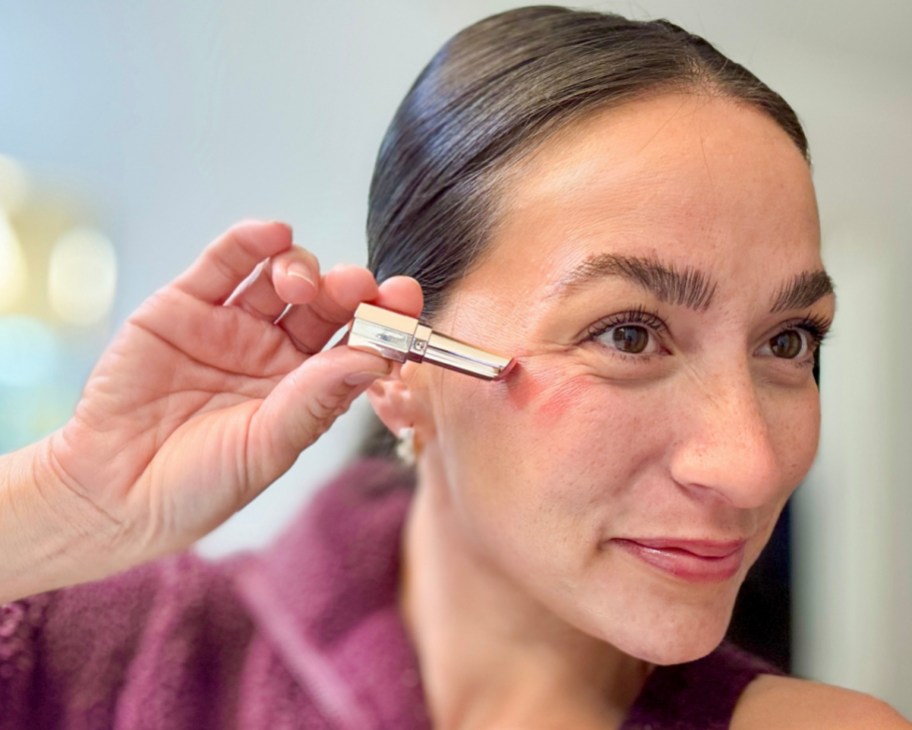 woman applying lipstick as blush on cheek