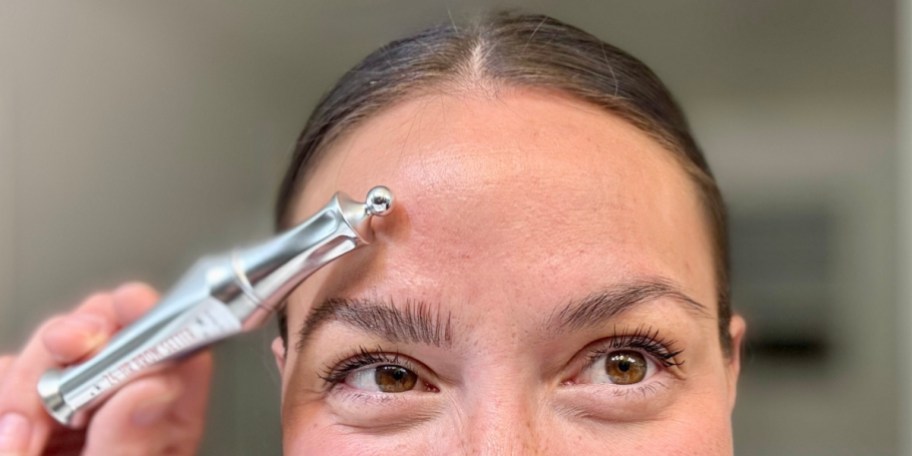 woman holding brow gel up to one eyebrow