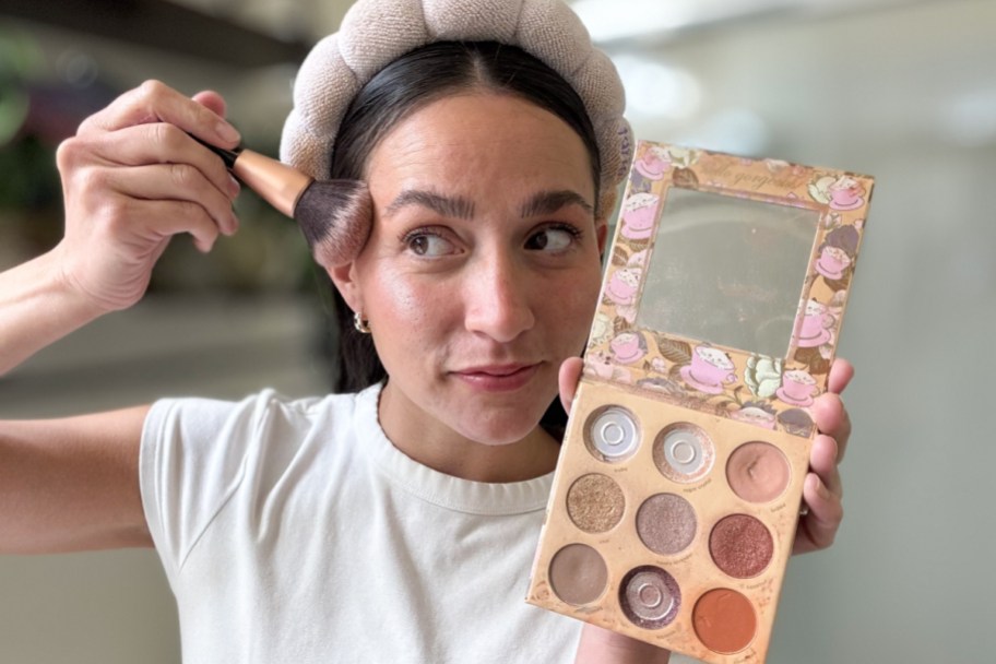 woman holding makeup palette swiping brush on cheek