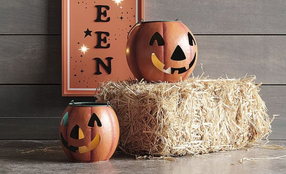 two metal jack o lanterns next to a bail of hay