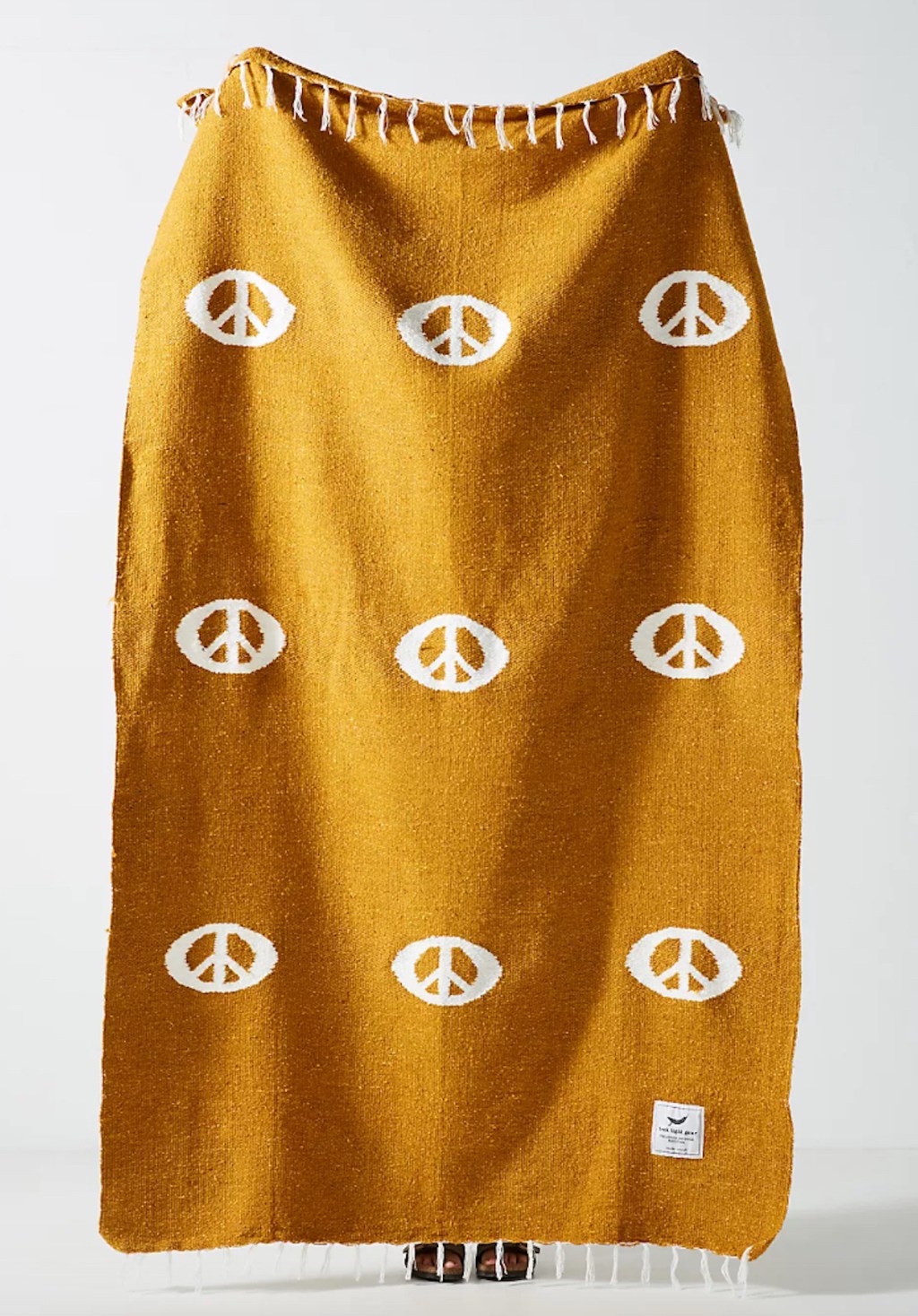 mustard colored peace sign anthropologie blanket being held up in white room