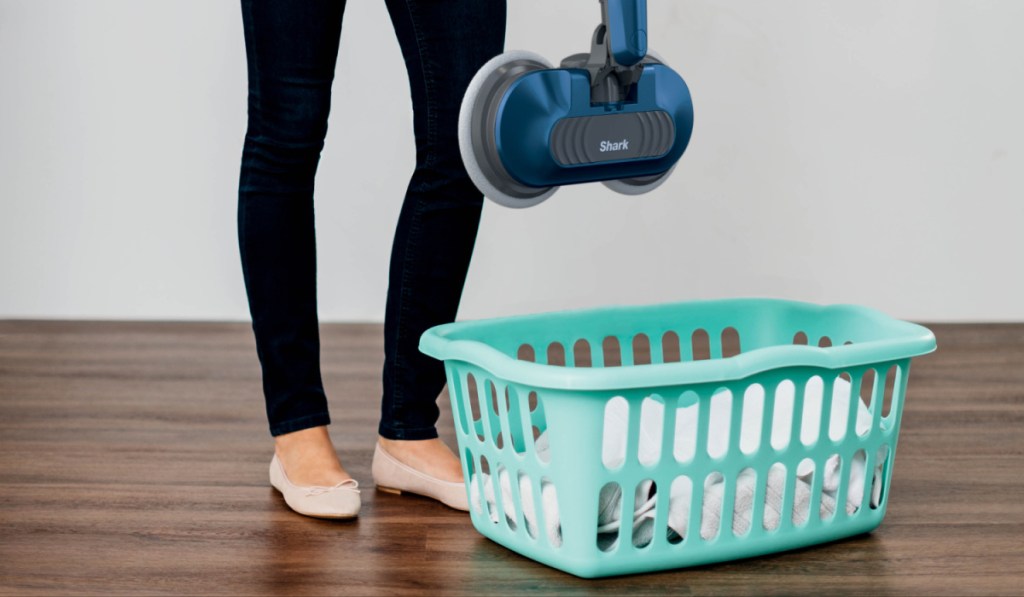 woman holding a shark steam mop over a teal laundry basket