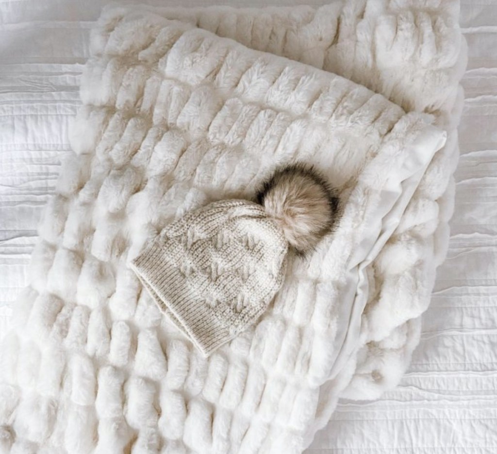 white ruched faux fur fabric with winter beanie laying on bed