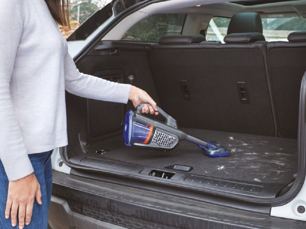 woman vacuuming pet hair from trunk of car