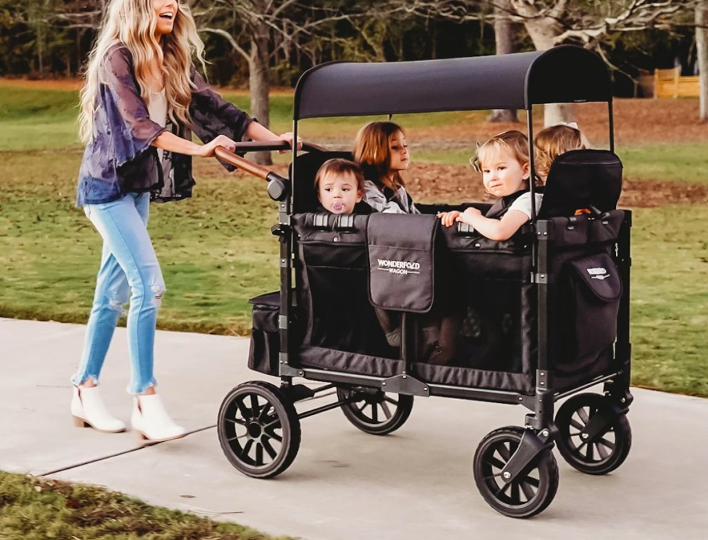 woman pushing wonderfold wagon on sidewalk with kids inside