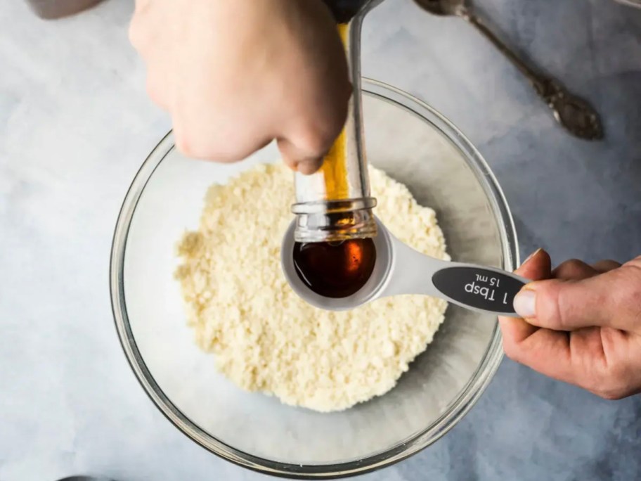 person filling measuring spoon with vanilla over bowl of flour