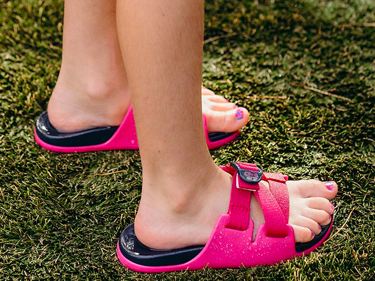 legs of a young girl wearing a pair of pink Chico Slides, standing on grass
