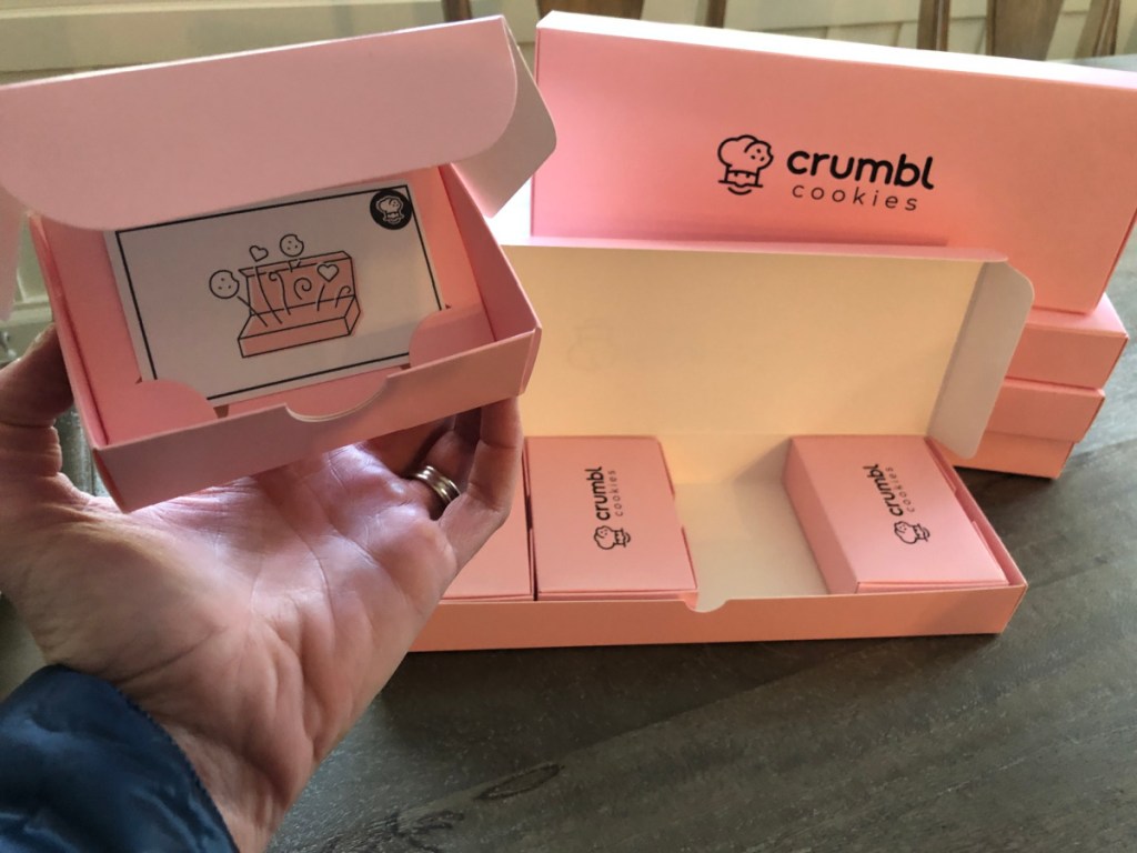 person holding up box with crumbl cookie gift card