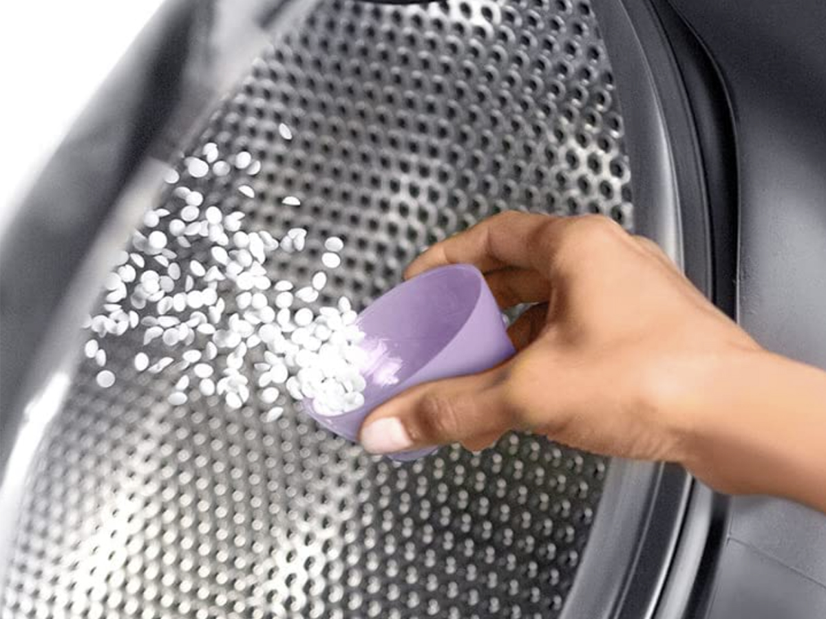 hand tossing downy light beads scent boosters from a cap into a dryer