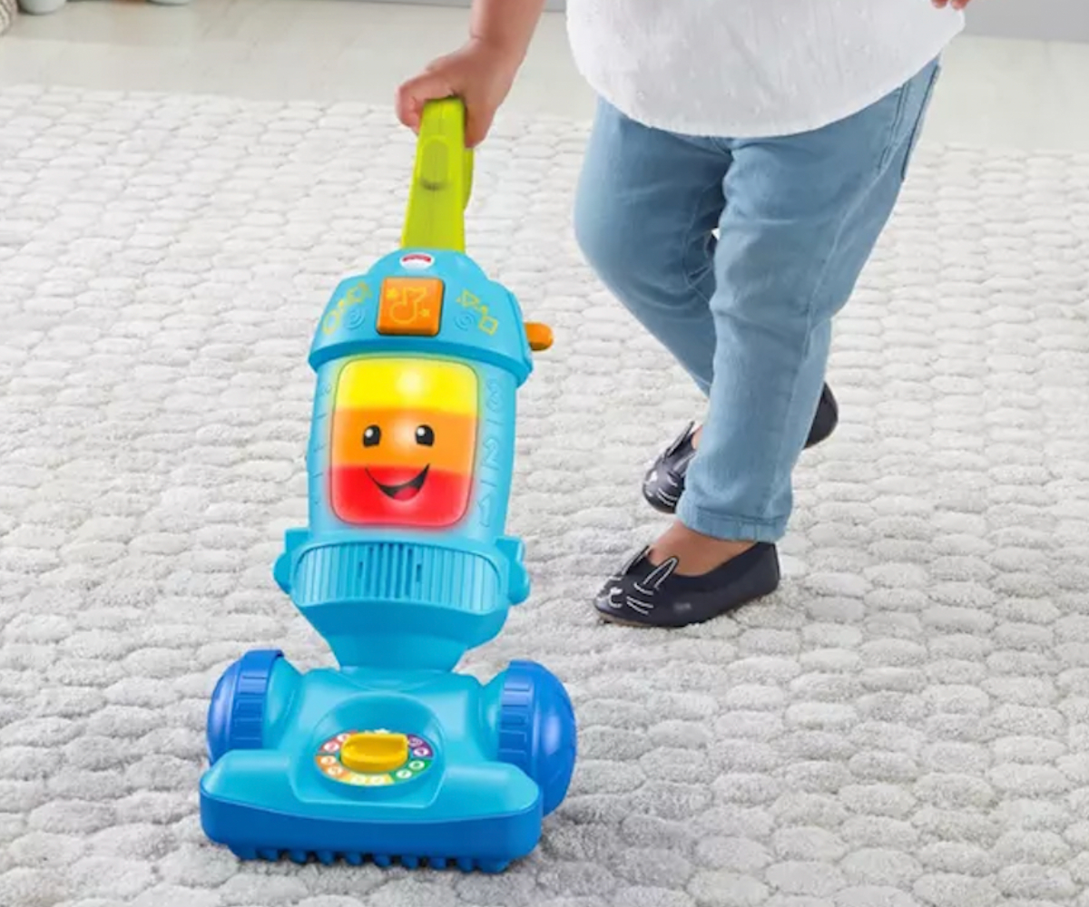 child pushing a Fischer Price toy Vacuum on a carpeted floor