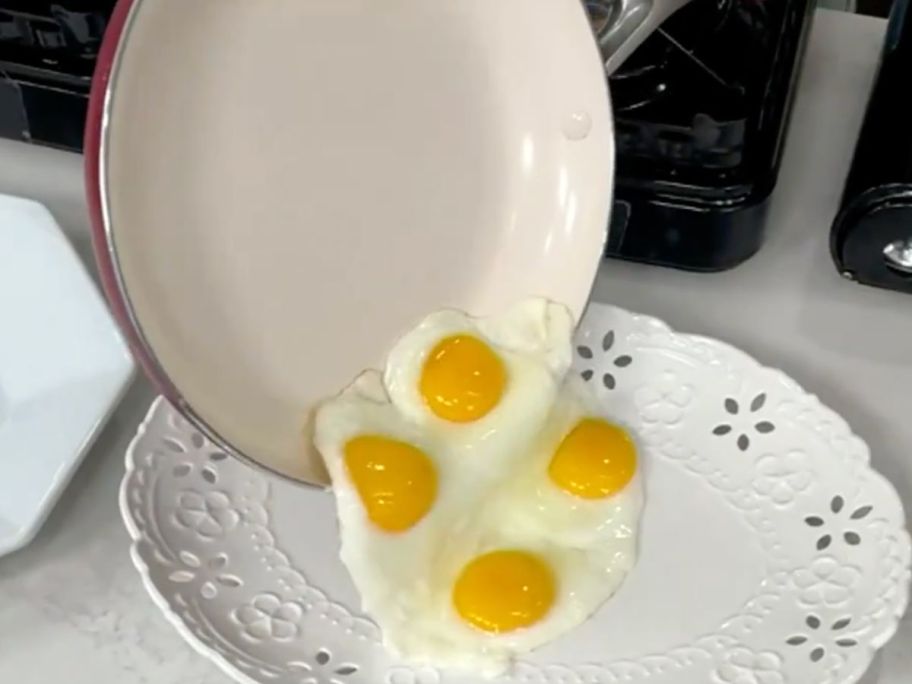 Greenpan frying pan with sunny side up eggs being slipped out of it onto a plate