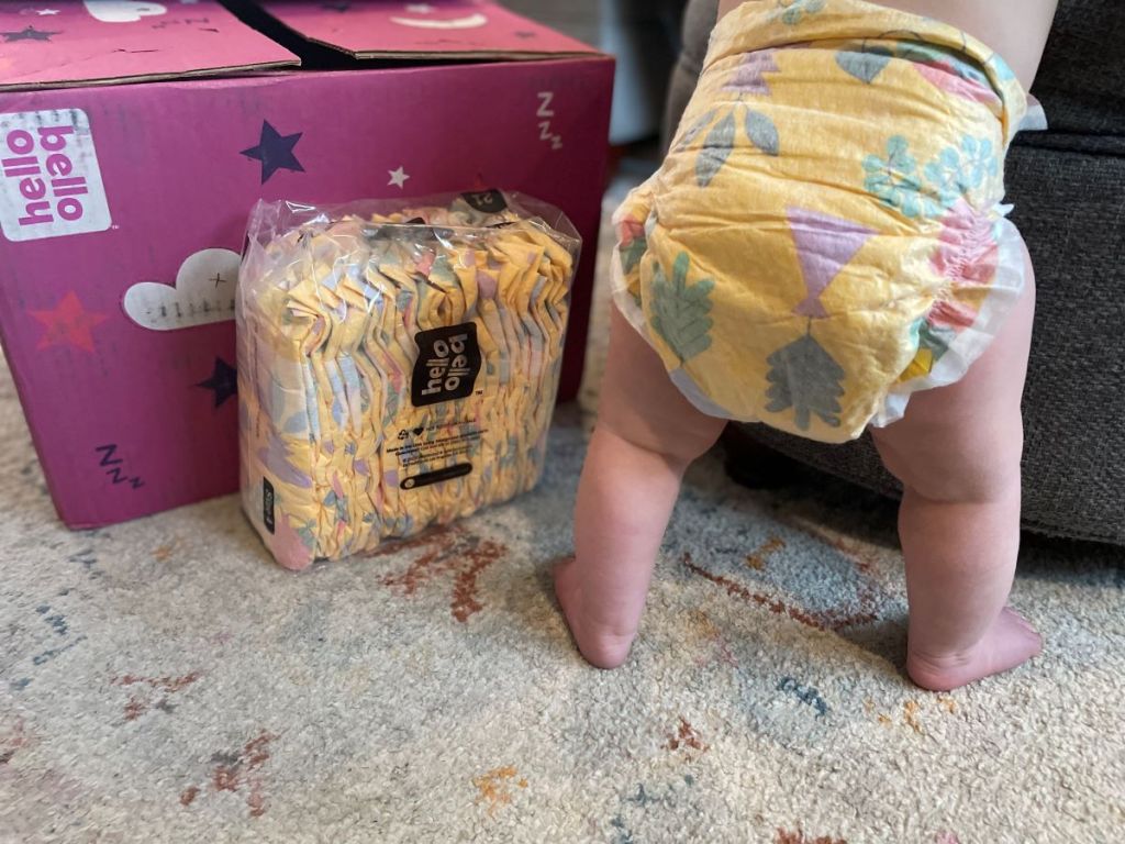 Baby standing next to a box of Hello Bello diapers