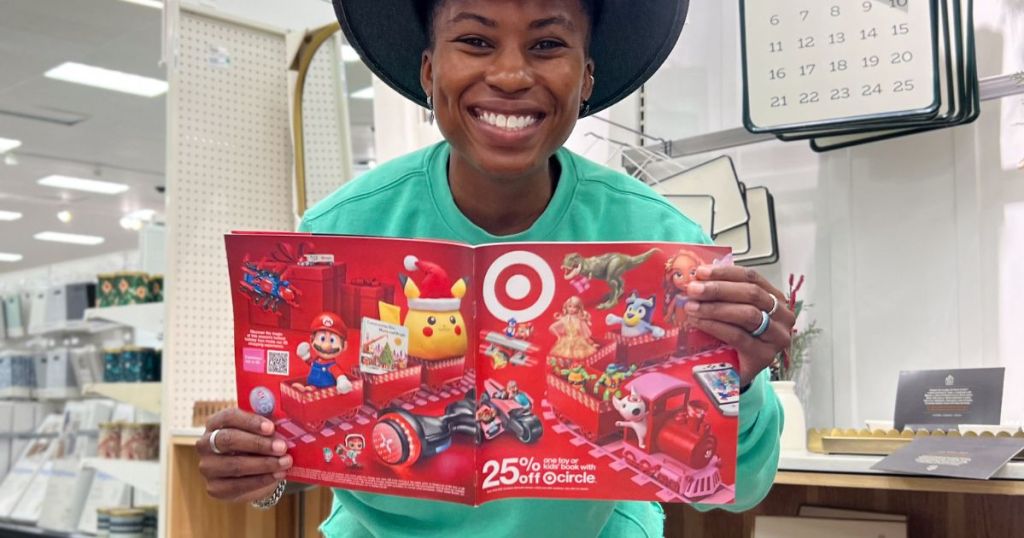 Cam smiling and holding up a Target's 2023 Holiday Toy Catalog