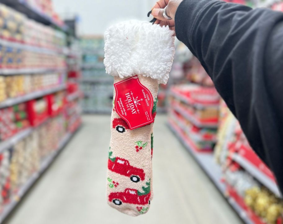 a womans hand holding a pair of christmas tree truck slipper socks