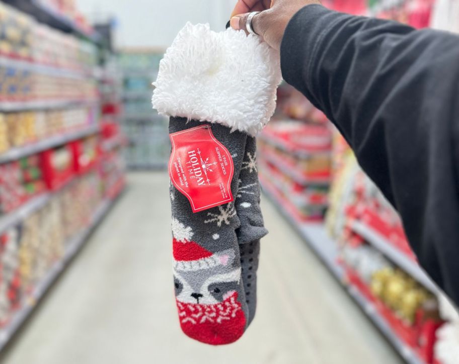 a womans hand holding a pair of raccoon slipper socks