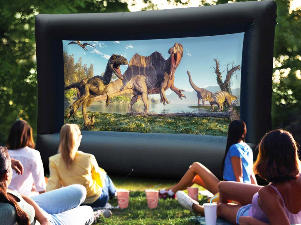 family watching dinosaur movie on outdoor screen in yard