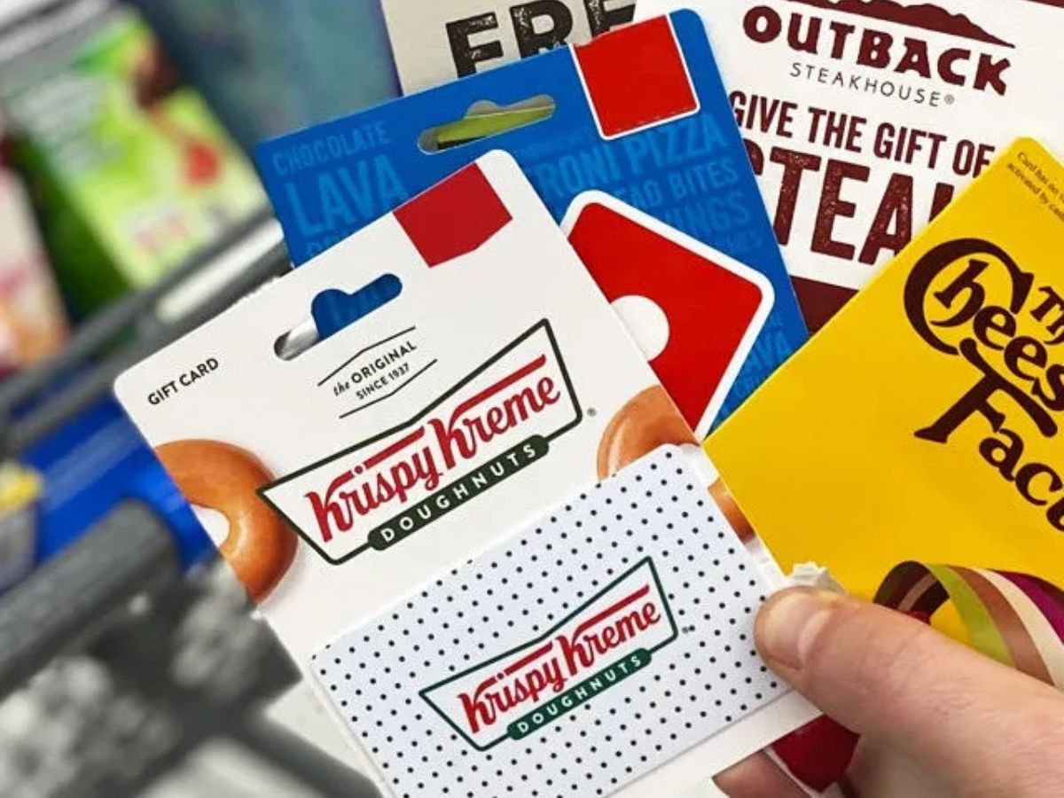 Hand, die eine Krispy Kreme-Geschenkkarte hält, mit anderen Restaurant-Geschenkkarten dahinter
