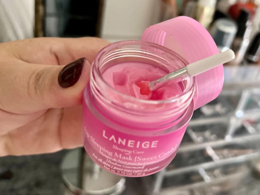 person holding jar of Laneige Lip Sleeping Mask pink color that's open with an applicator in it