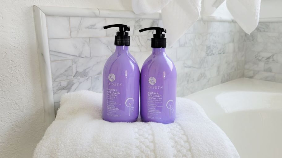 Luseta Shampoo Conditioner purple bottles sitting on towel by a tub