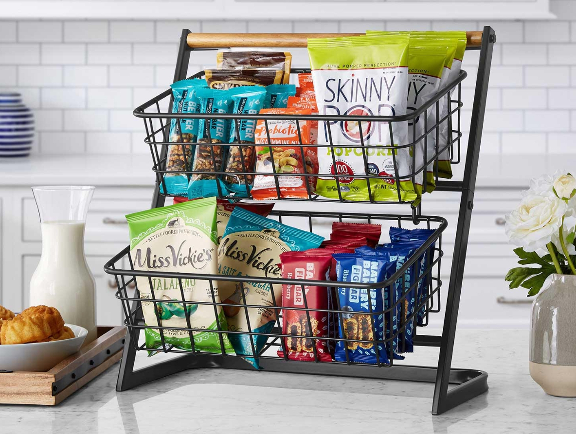Two tier baskets holding snacks like chips, popcorn, snack bars, and dried fruit.