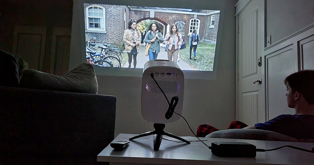 mini projector on table with person watching movie on wall