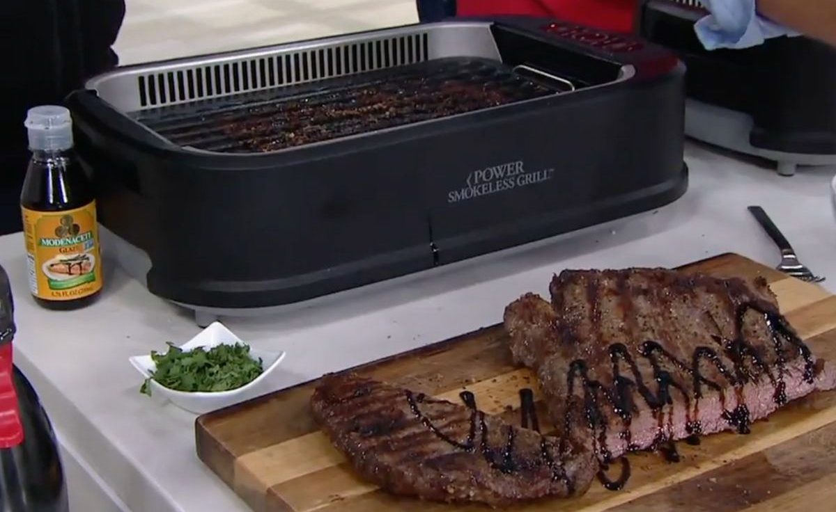 PowerXL Smokeless Grill with a cooked flank steak in front of it on a cutting board