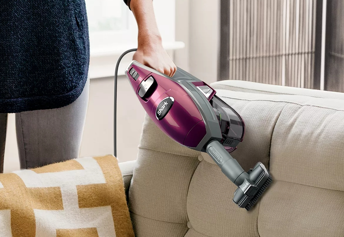 person using the Shark rocket Vacuum handheld to clean the back of a couch in a living room