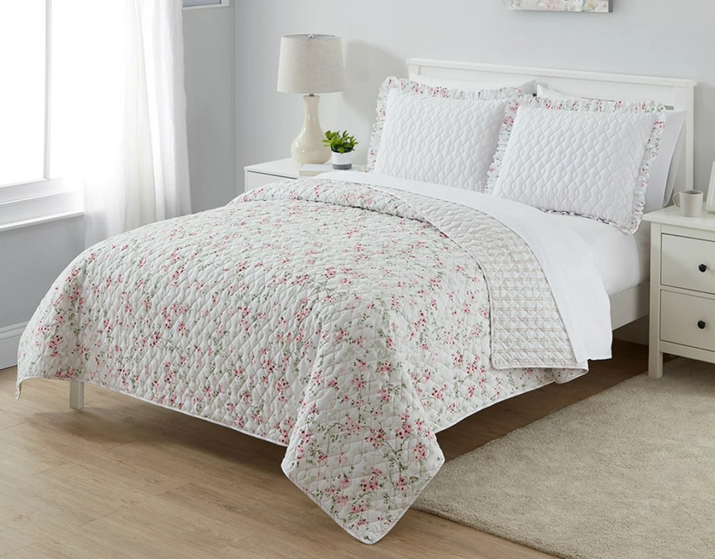 Bed with a white floral quilt on it