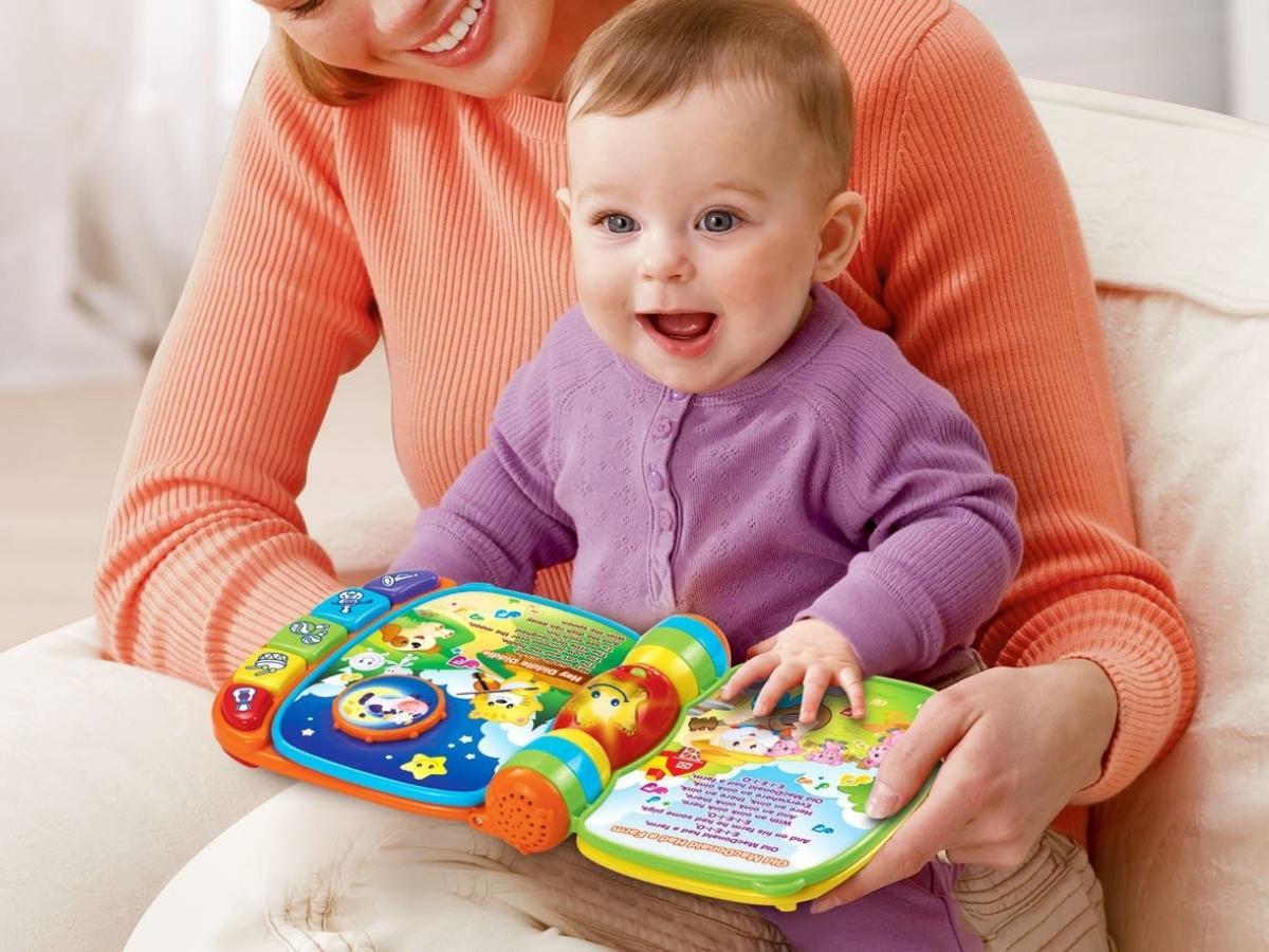 woman holding a baby playing with the VTech Musical Rhymes Book