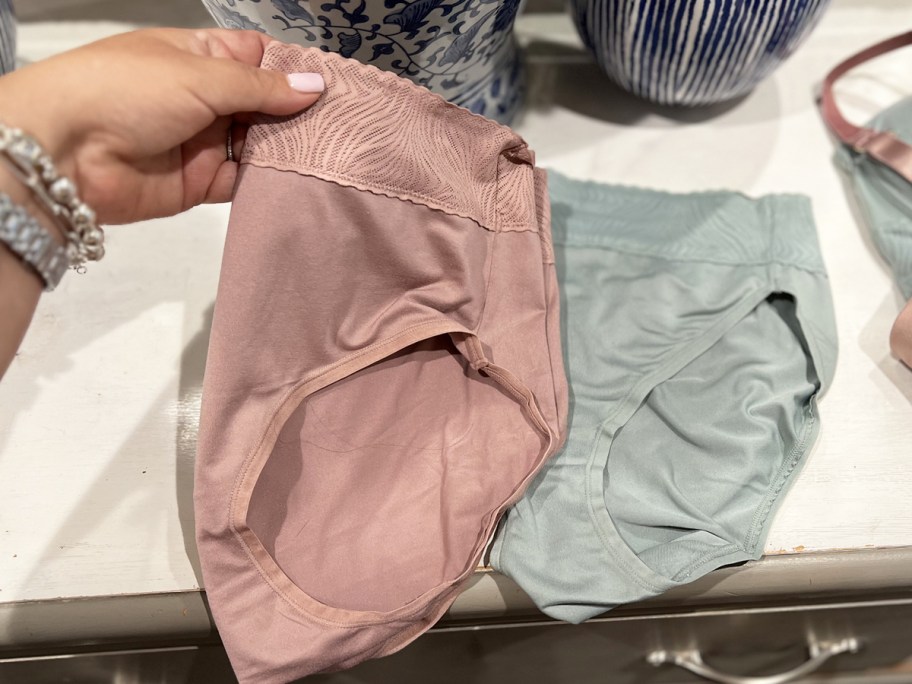 hand holding up pink pair of underwear from dresser