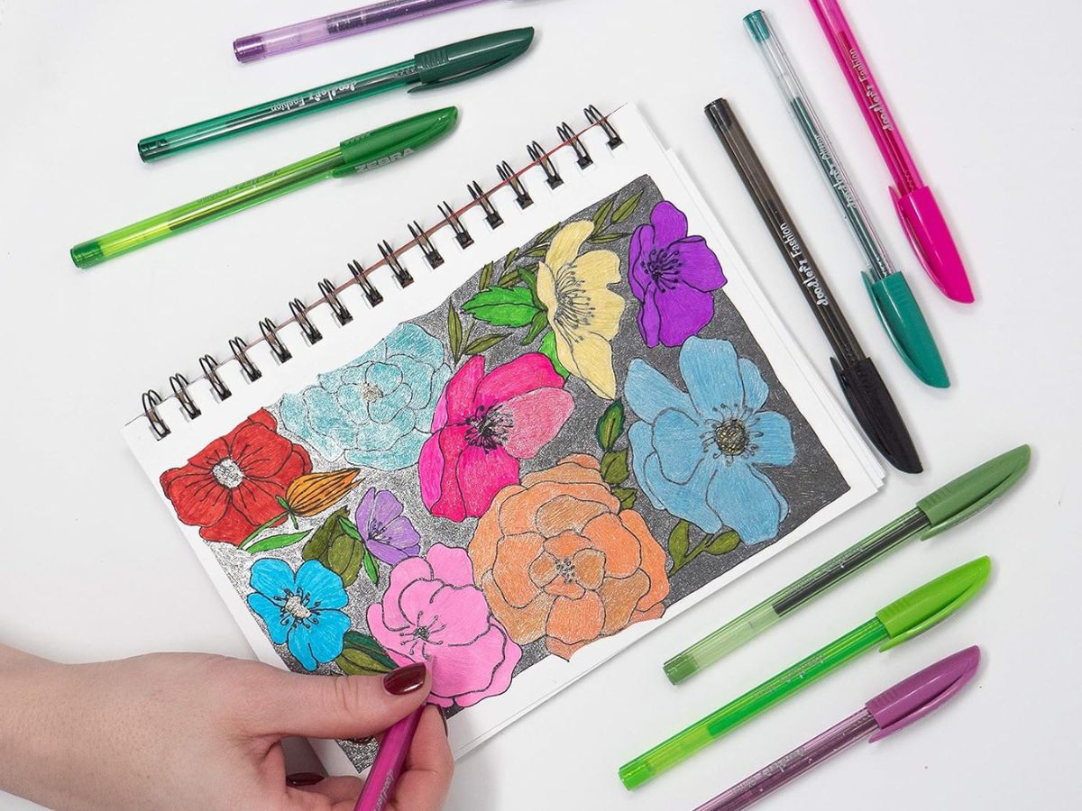 colorful pens surrounding notebook that someone is drawing flowers in