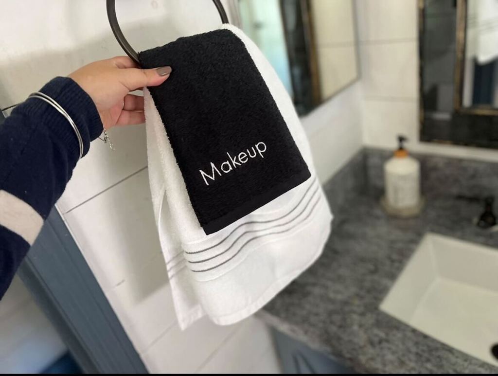 hand holding hand towels in bathroom with makeup logo
