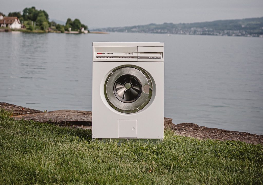 white front load washer sitting outside in grass by water