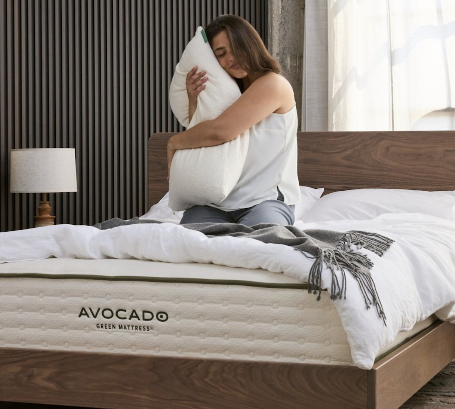 woman sitting on bare avocado mattress hugging white pillow