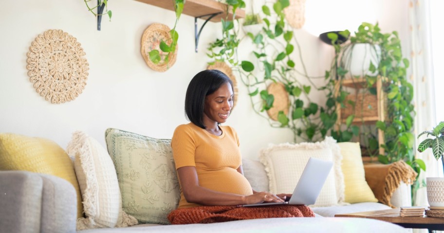 pregnant woman sitting on couch with laptop smiling