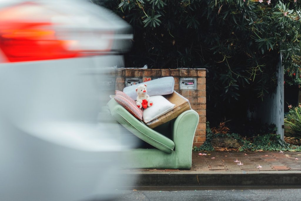 car driving by green sofa and trash on curb