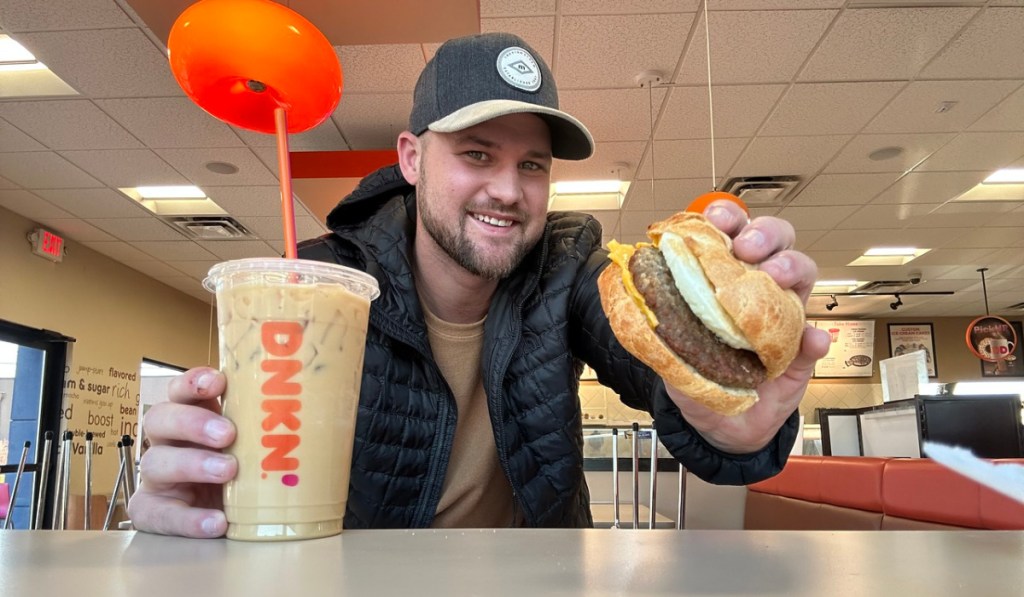 man holding dunkin donuts sandwich and drink