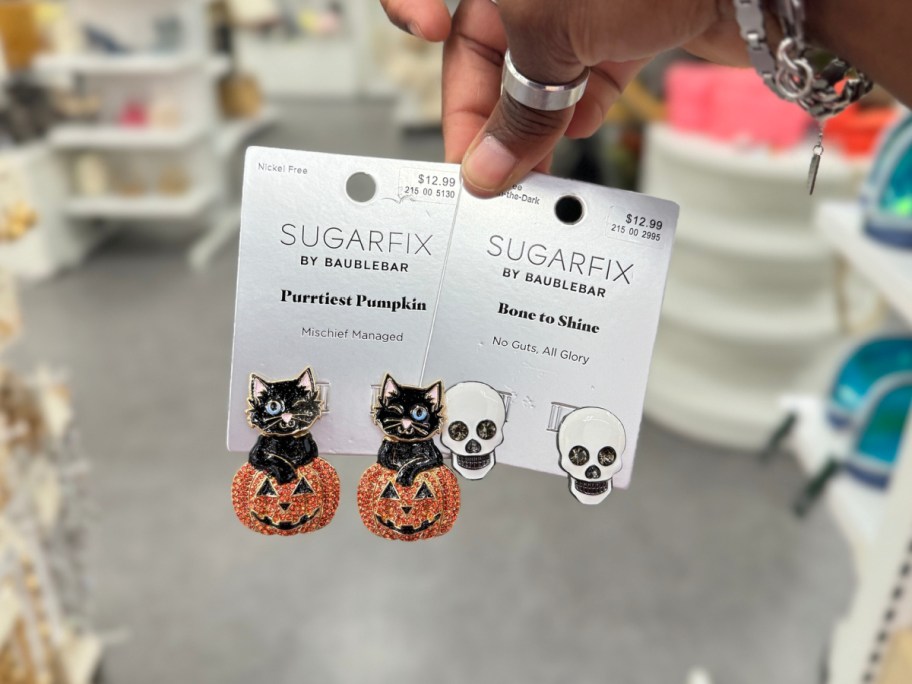 hand holding halloween pumpkin and skull drop earrings