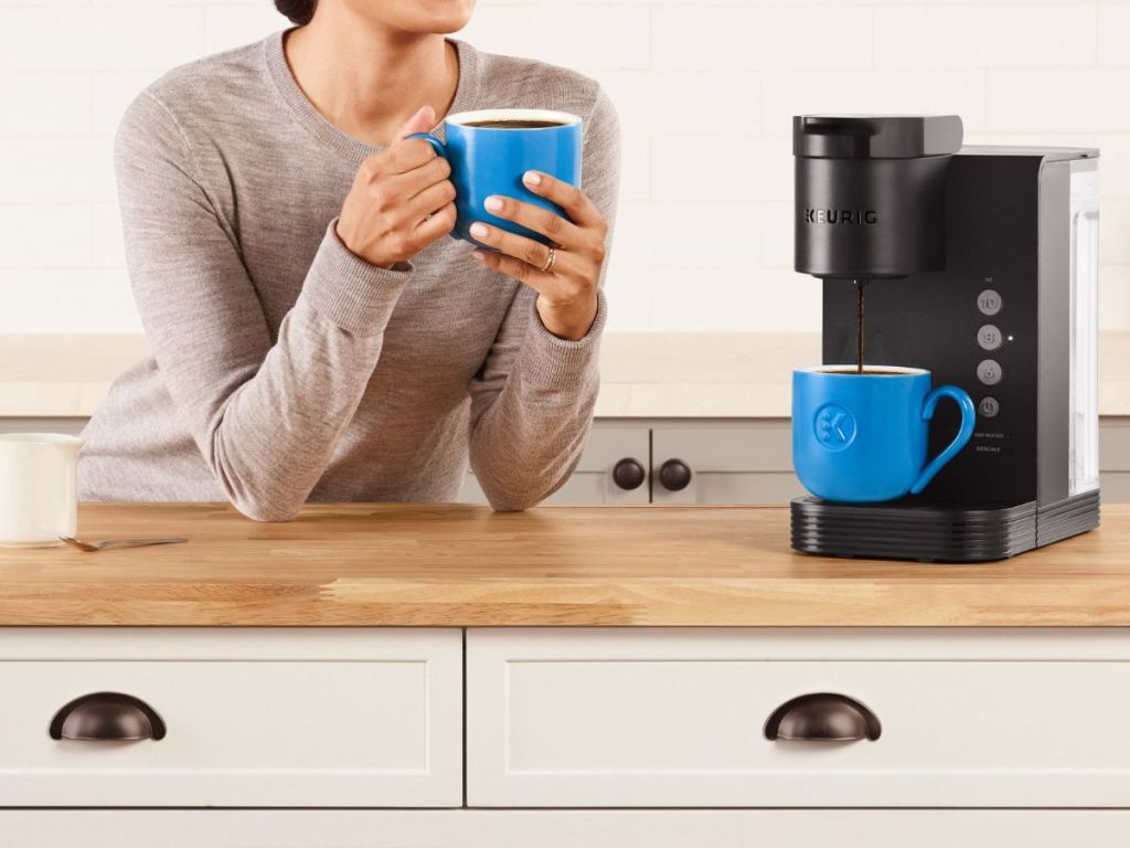 woman holding coffee mug by Keurig machine
