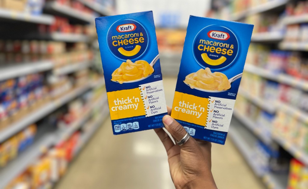 hand holding up two boxes of kraft mac cheese in a store aisle