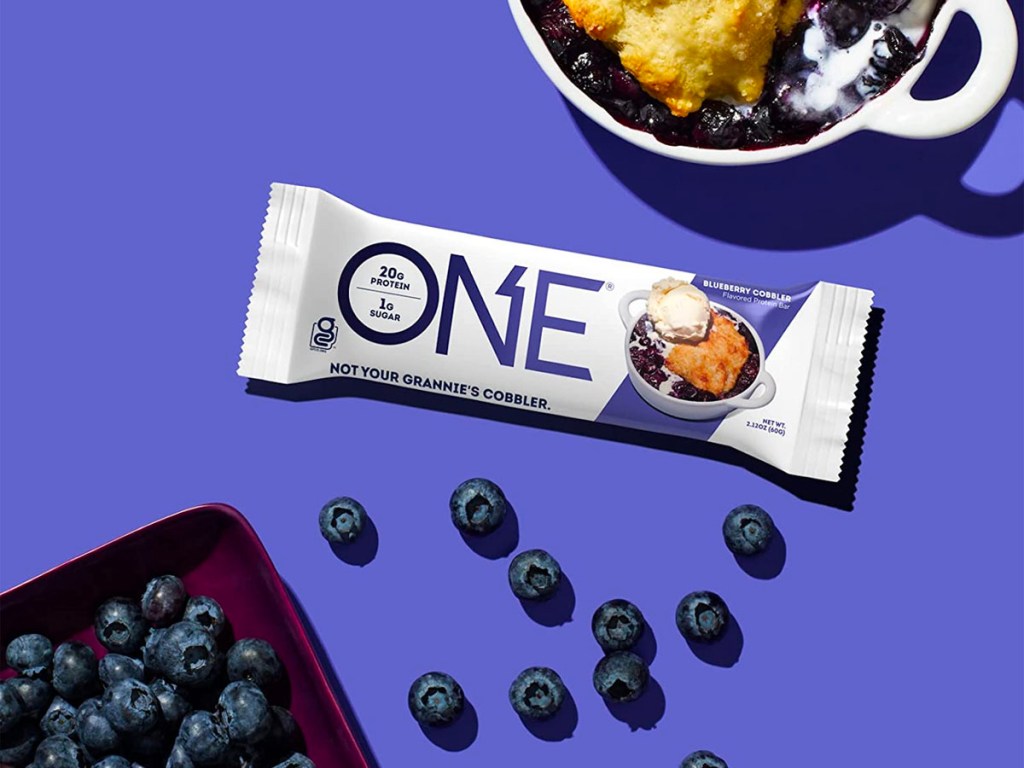 protein one blueberry cobbler bar next to bowl of blueberry cobbler and blueberries