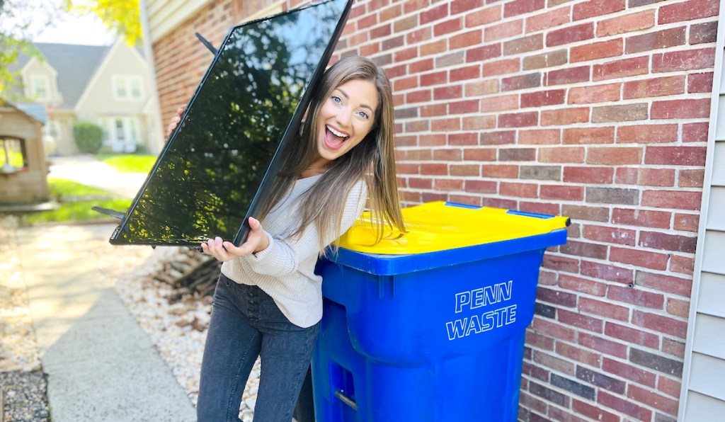 woman holding tv standing next to recycling bin