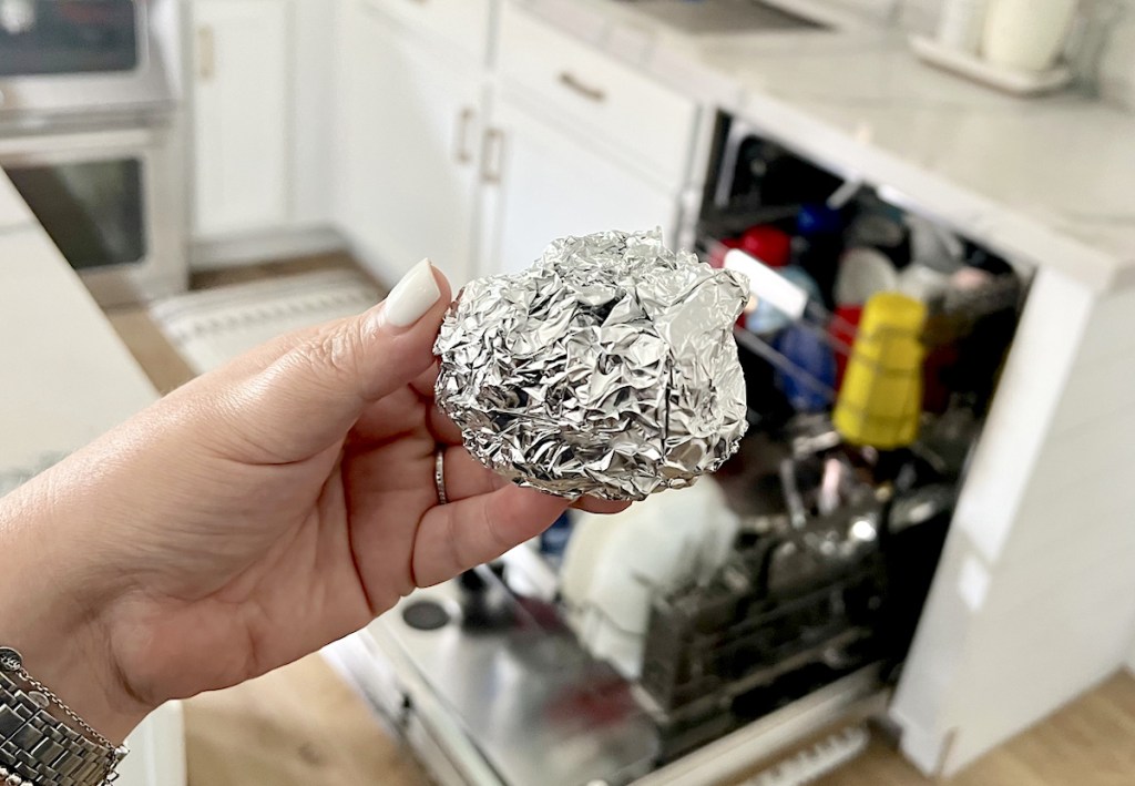 hand holding an aluminum foil ball over dishwasher