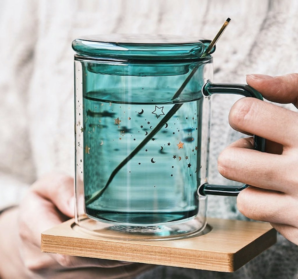 hand holding blue stars glass coffee mug on wood coaster