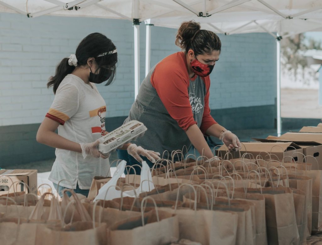 woman with teen putting food in brown bags for food drive
