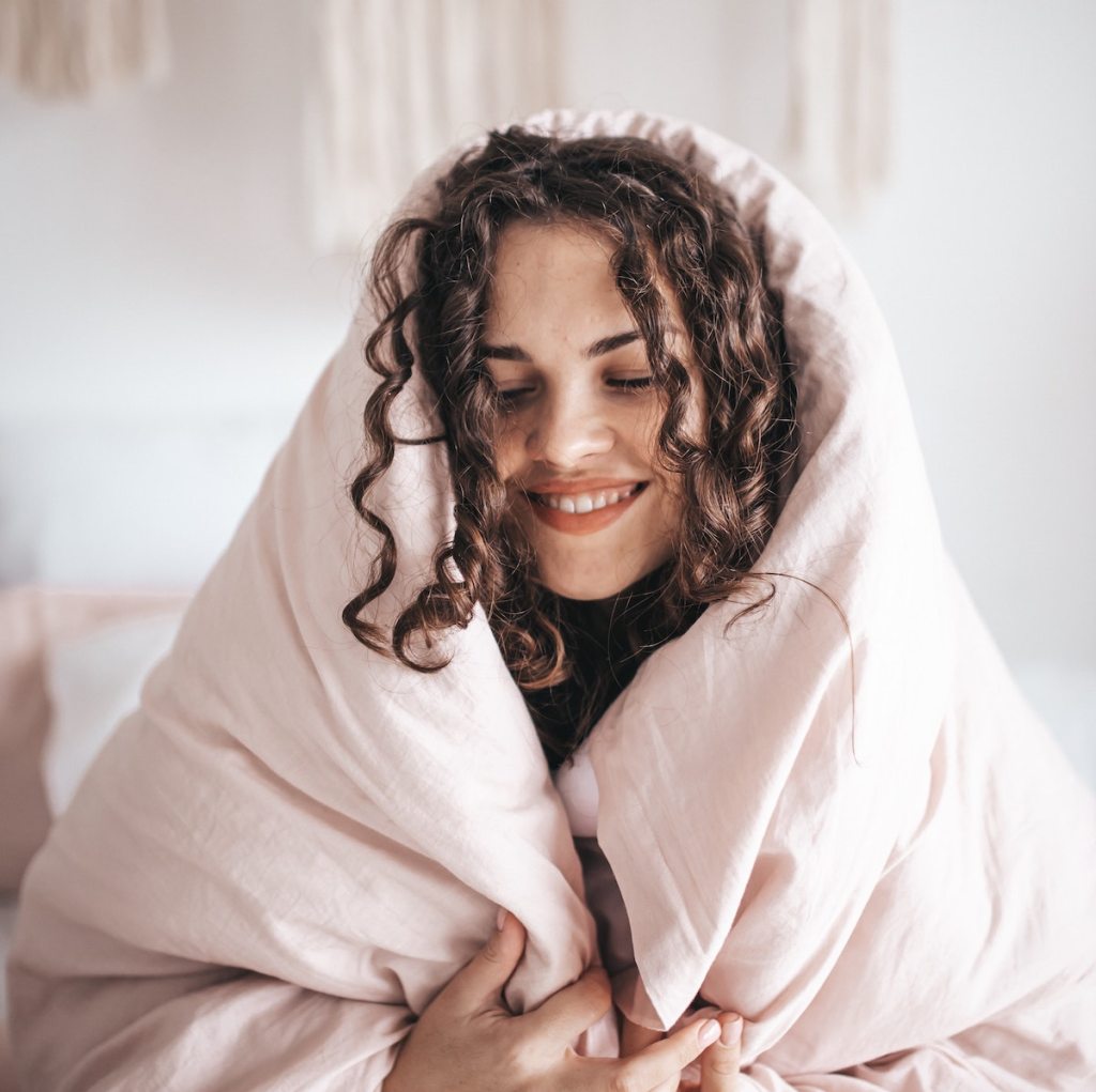 woman smiling with eyes closed wrapped in light pink blanket