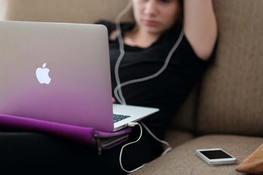 teenager sitting on couch with apple laptop on lap and phone on couch