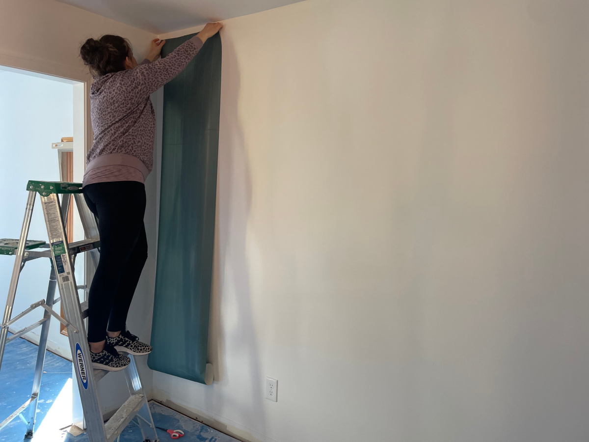 woman on step ladder adding wallpaper to walls